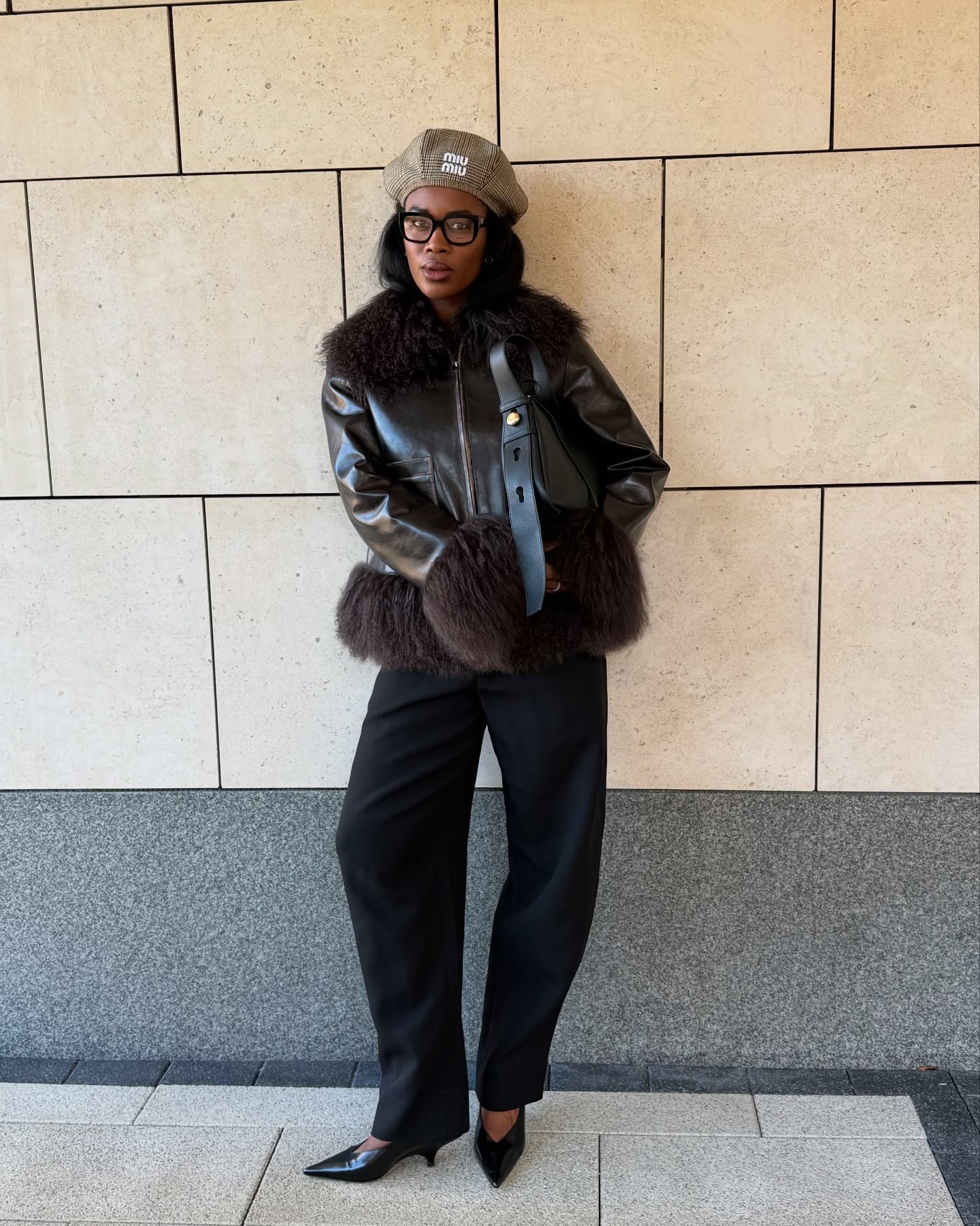 Marilyn wears a miu miu hat, fur-trimmed leather jacket, black pants, and v-cut vamp heels.