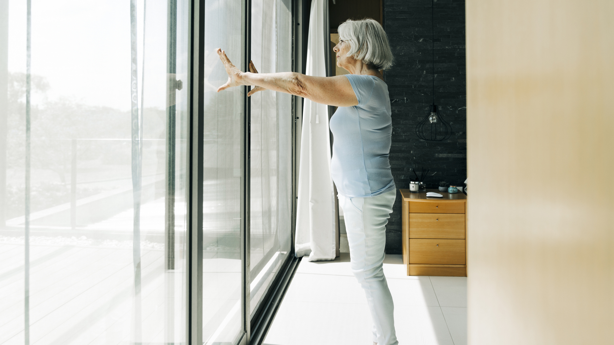 Woman standing in front of sliding glass doors, with her hands on the glass at shoulder height