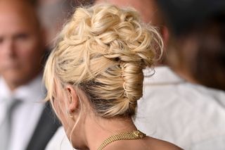 A photo of Millie Bobby Brown securing her braided blonde bun with a set of gold hair pins.