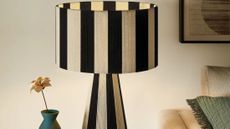 Striped table lamp pictured alongside a teal bud vase inside of an ambient living room