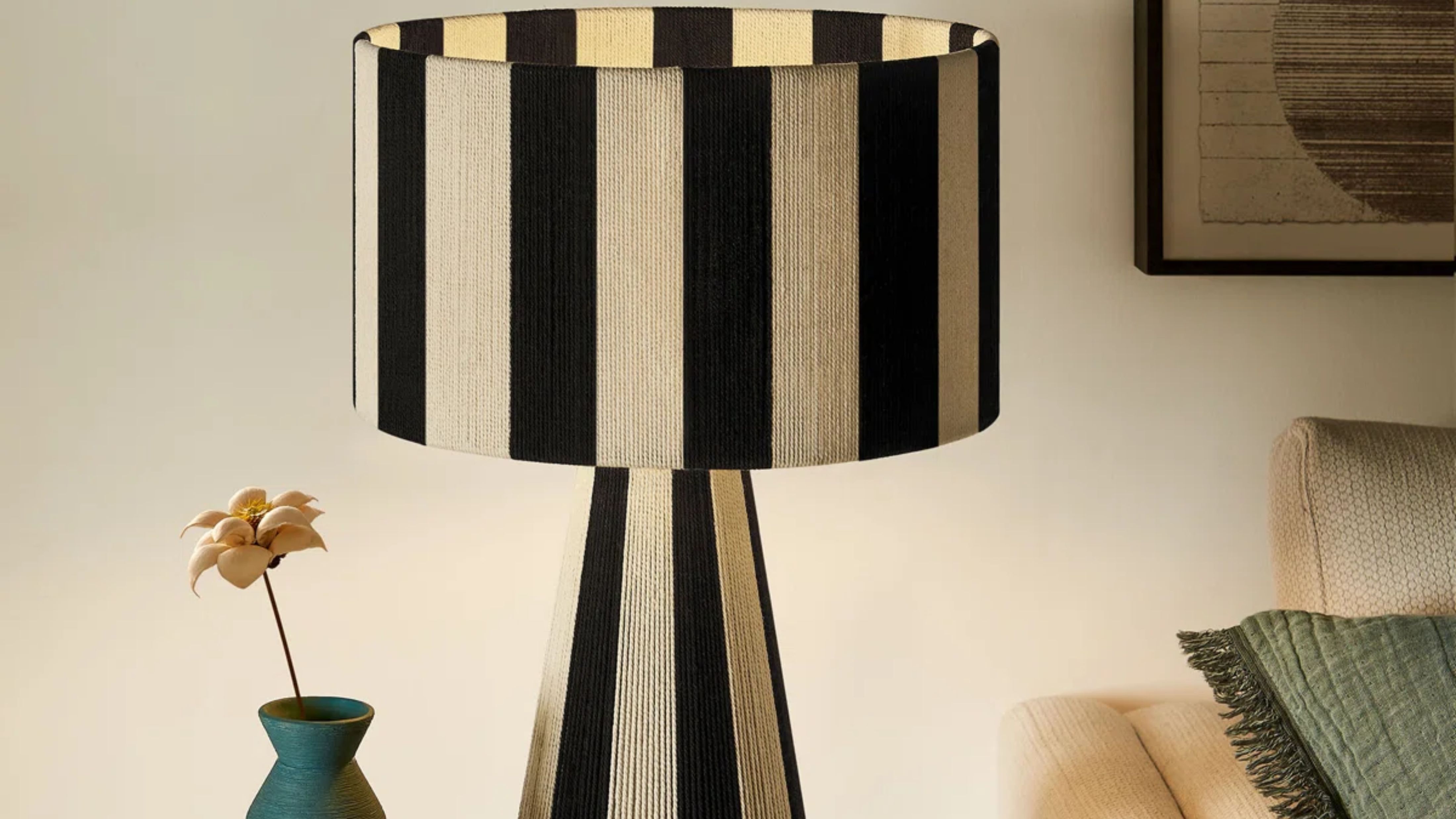 Striped table lamp pictured alongside a teal bud vase inside of an ambient living room