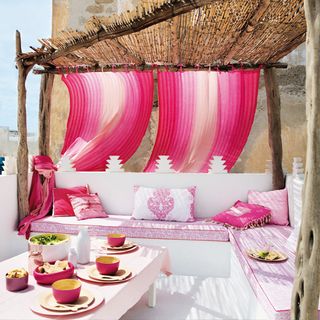 Outdoor seating area with white benches, bamboo canopy, pink cushions and low table