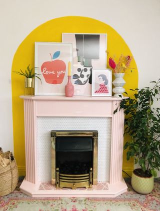 pink fireplace in a living room with a yellow arched wall and art prints