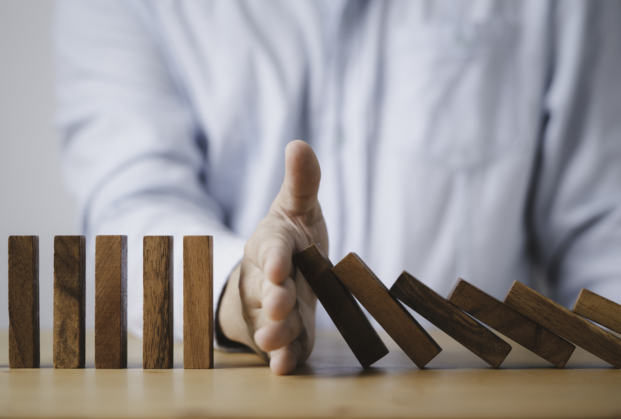 Businessman hand stop wooden block falling others block dominos for risk and crisis management concept.