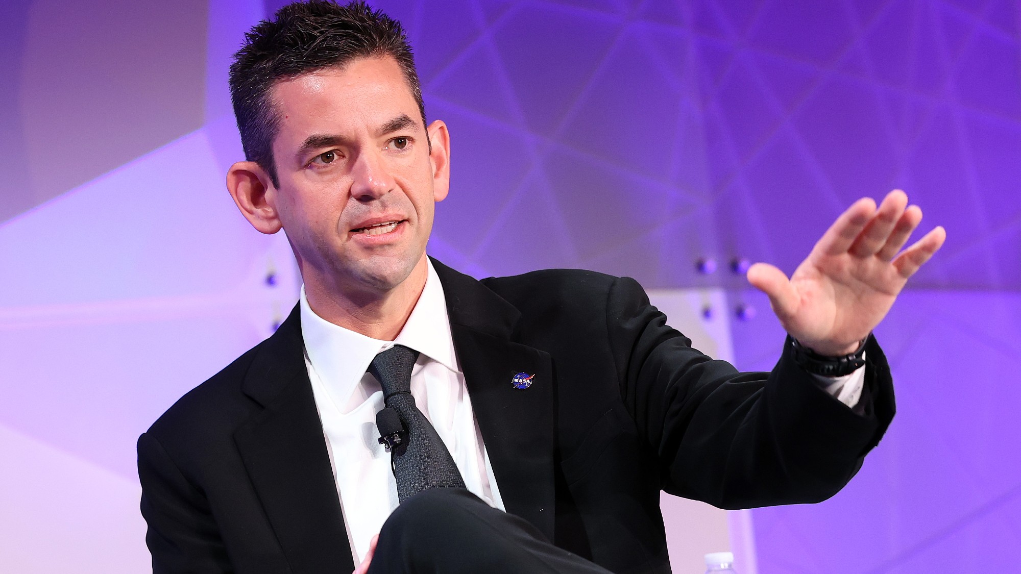 a man in a suit and a NASA pin speaks on stage