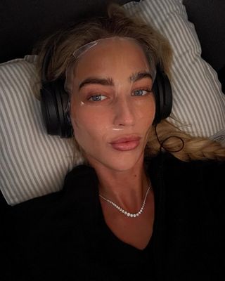 Emili Sindlev wearing a sheet face mask and headphones on a flight.