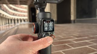 A thumb pushes the mini joystick on the rear of the gimbal to make the smartphone’s camera tilt and pan