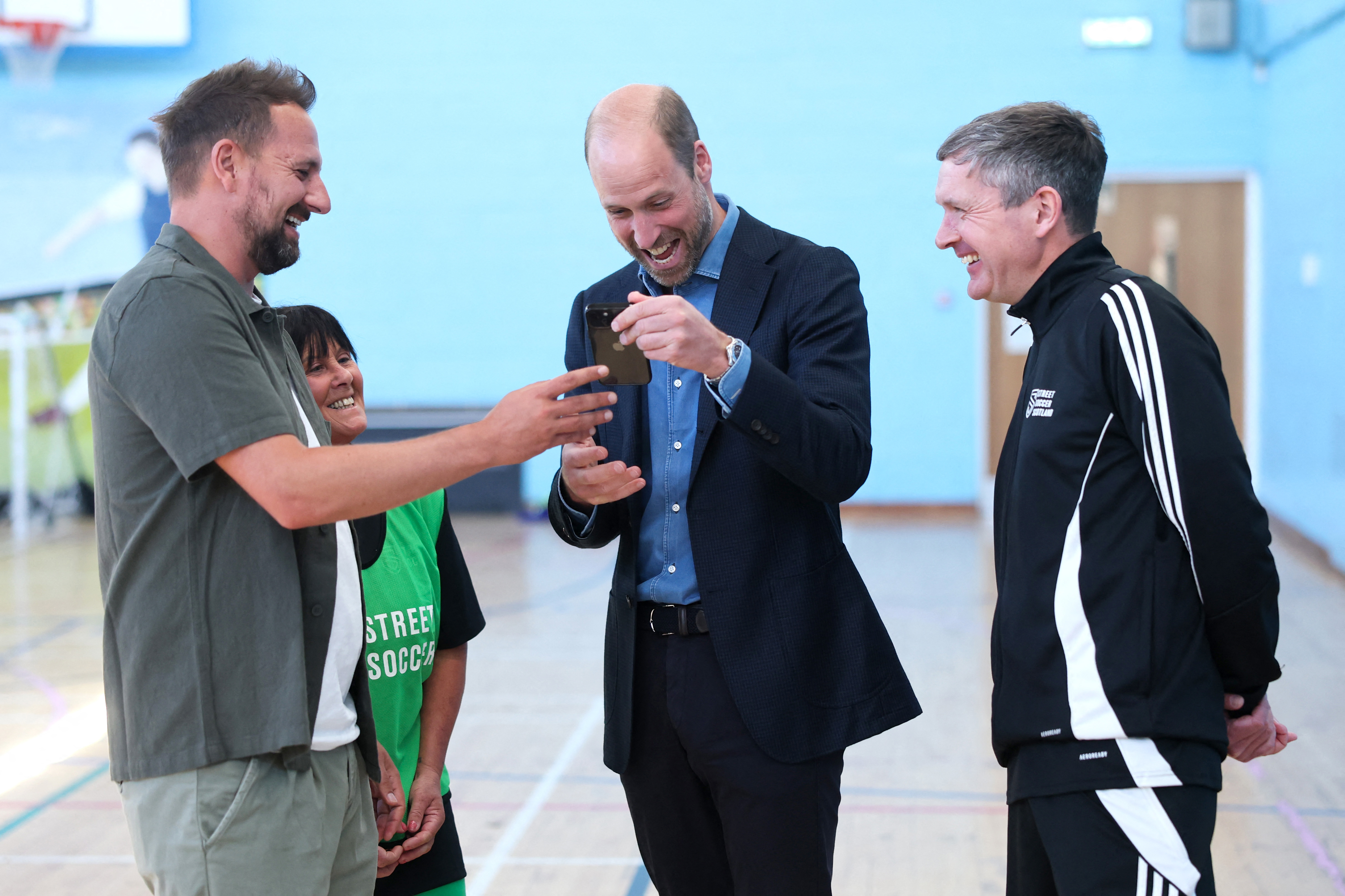 Prince William looking at a man's phone and smiling in a gym
