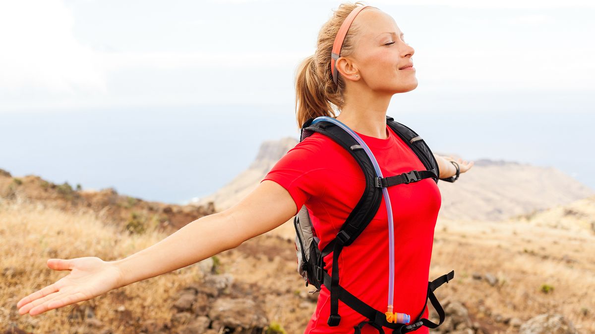 A woman runner stretching out her arms on a grassy hilltop.