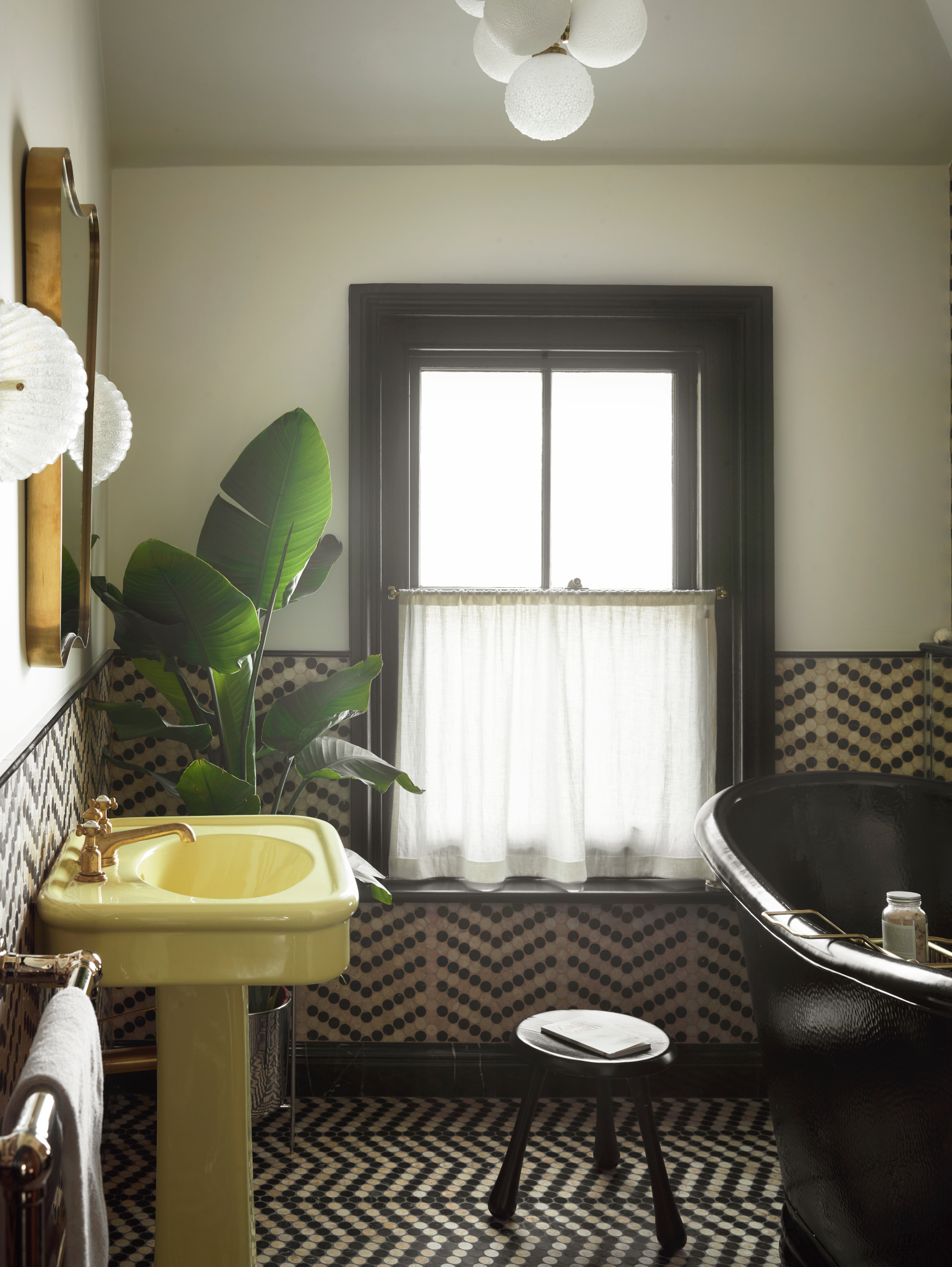 Bathroom with black and beige mosaic tiles, yellow sink, black bath and black stool, plus large palm plant