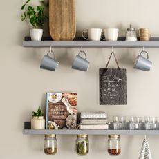 Two floating kitchen shelves with cup hooks and blue mugs, chopping board and blackboard, with storage jars with lids fixed below shelves