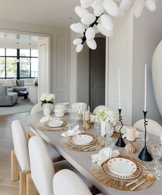 Dining table setting with layered plates, candleholders, vases of fresh flowers and tableware