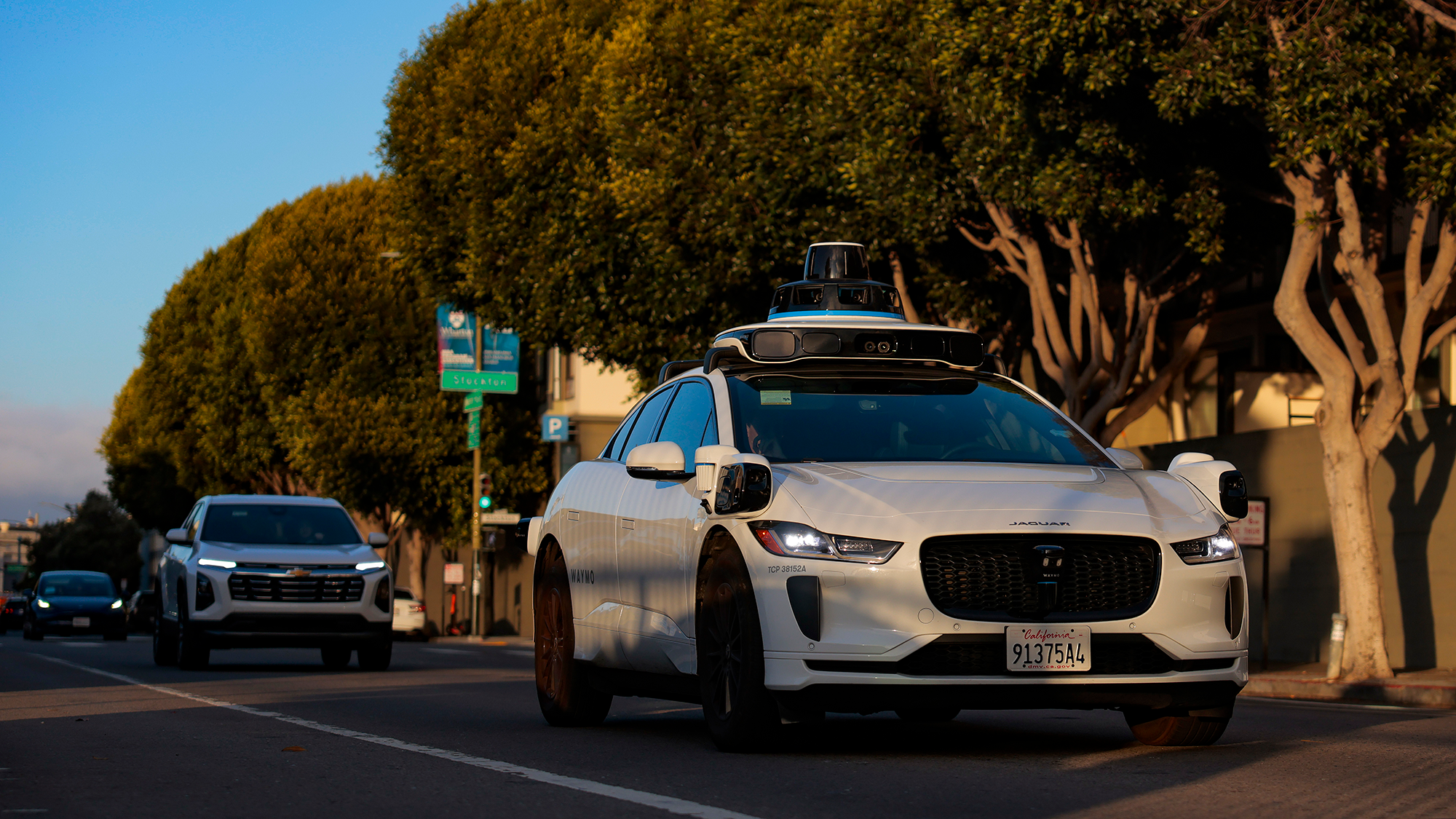 A car with a camera on top drives down a busy road.
