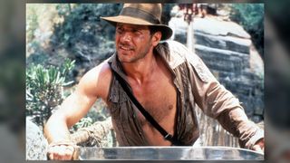 Harrison Ford wears his iconic Indiana Jones hat and an open jacket missing a sleeve.