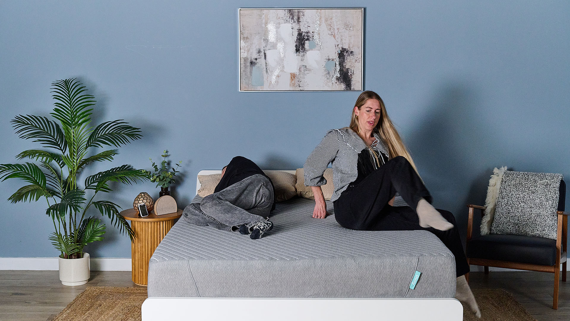 This image shows our subjective motion isolation test, conducted in our sleep studio. The Siena Memory Foam Mattress sits on a bed frame in the middle of a decorated room. Frances Daniels, a member of our sleep team, lies on the right side of the mattress in a side sleeping position. On the left of the bed, Nicola Appleton is climbing on the mattress using high force movement. Despite Nicola&#039;s movements, Frances looks undisturbed.