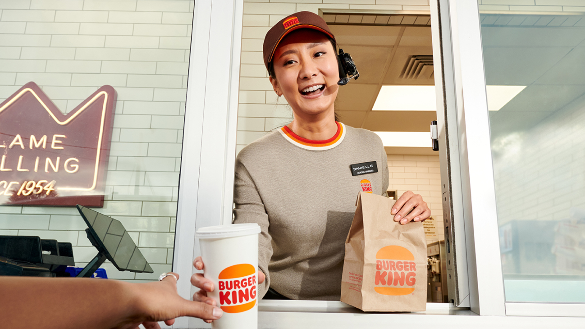 A Burger King employee at the drive-thru window handing a bag of food and a drink to a customer.