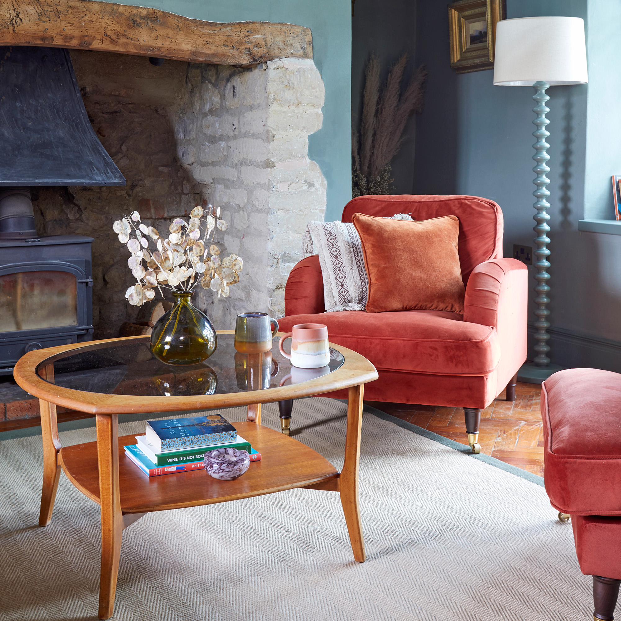 blue living room with red velvet sofas and wood and glass oval coffee table inglenook fireplace and wooden flooring with a cream rug