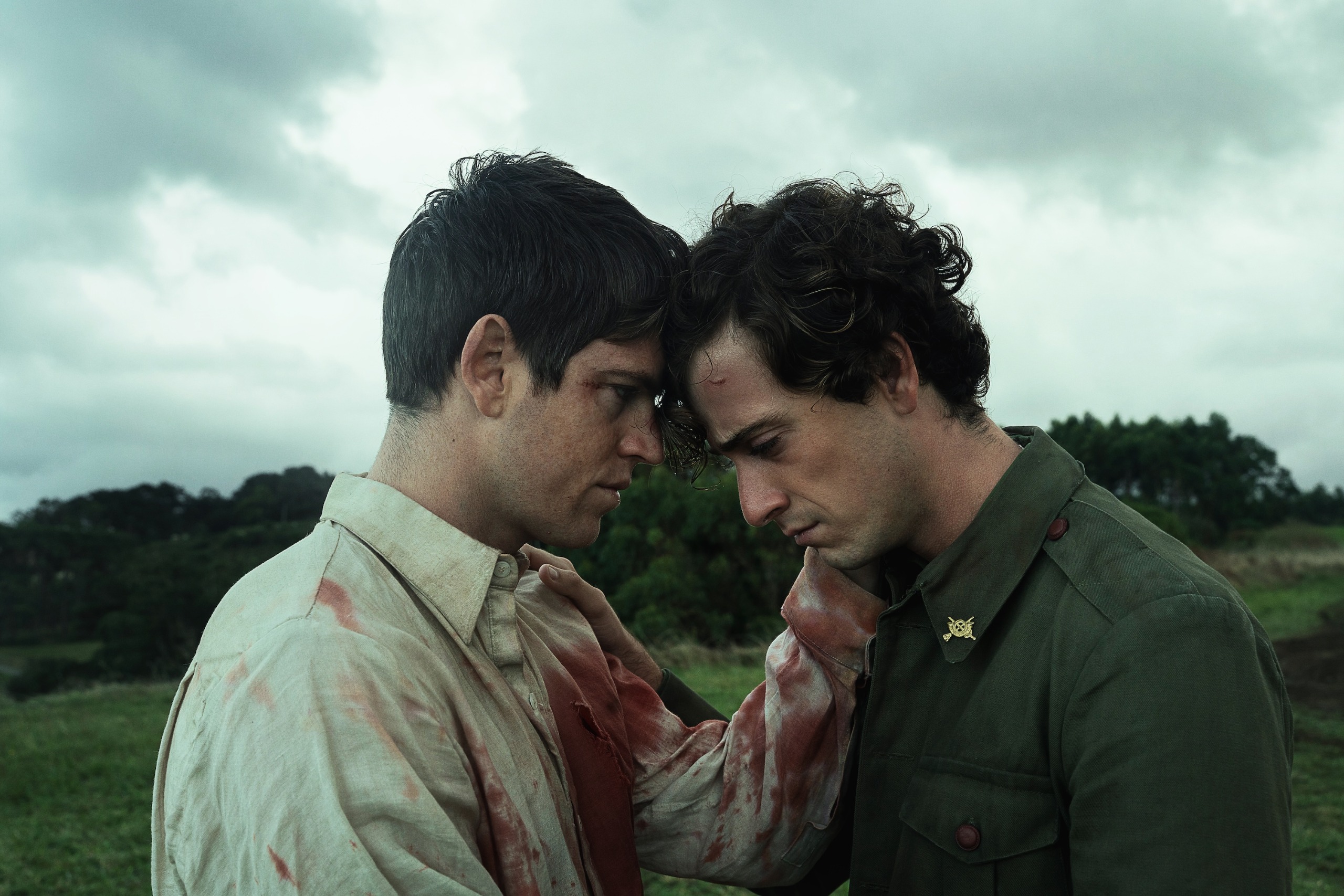 A man wearing a blood-splattered shirt (Miguel Bernardeau as Rafael) and a man in a military uniform (Guitarricadelafuente as Sebasti&amp;aacute;n) stand closely together in a green field, in 'La Bola Negra.'