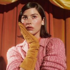 Gracie Abrams wearing Miu Miu gloves, sweater, and skirt posing with a puppet for Who What Wear's fall issue cover.