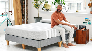 A happy customer sitting on the edge of a Leesa Mattress in his bedroom