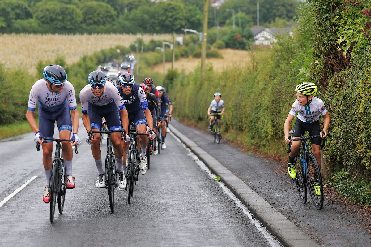 Picture by Alex Whitehead/SWpix.com - 06/09/2022 - Cycling - 2022 AJ Bell Tour of Britain - Stage 3: Durham to Sunderland, England - The Peloton lead by Reto Hollenstein and Mason Hollyman of Team Israel Premier Tech with a young fan riding along side the peloton