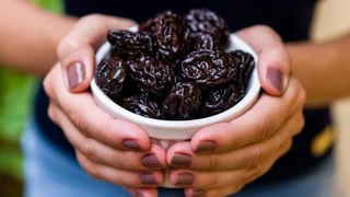Woman holding a bowl of prunes, which can help to build healthy bones