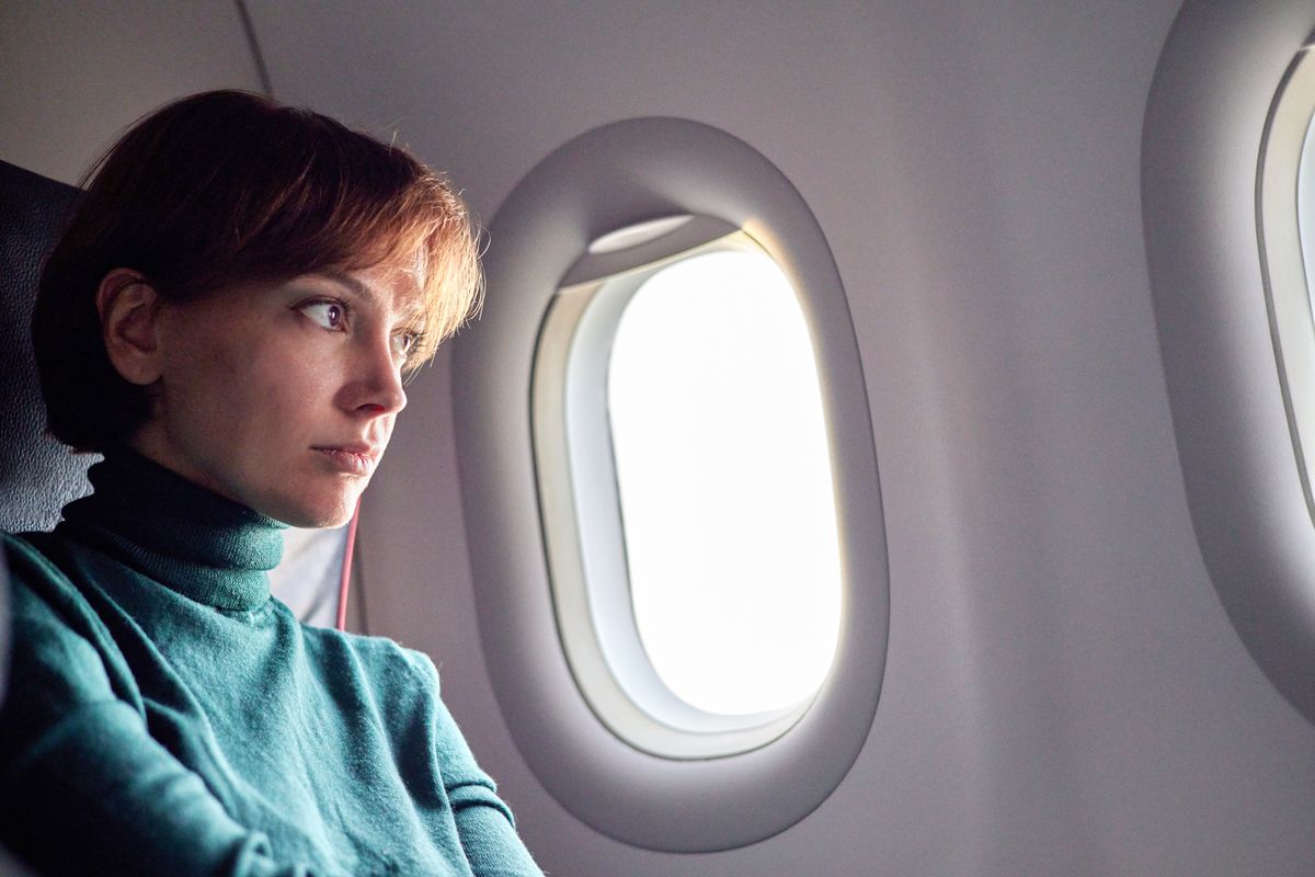 A woman sits awake on an airplane looking unhappy.
