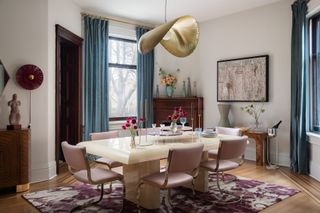 A dining room with pastel pink chairs, a large, gold-painted lighting piece, and long white table