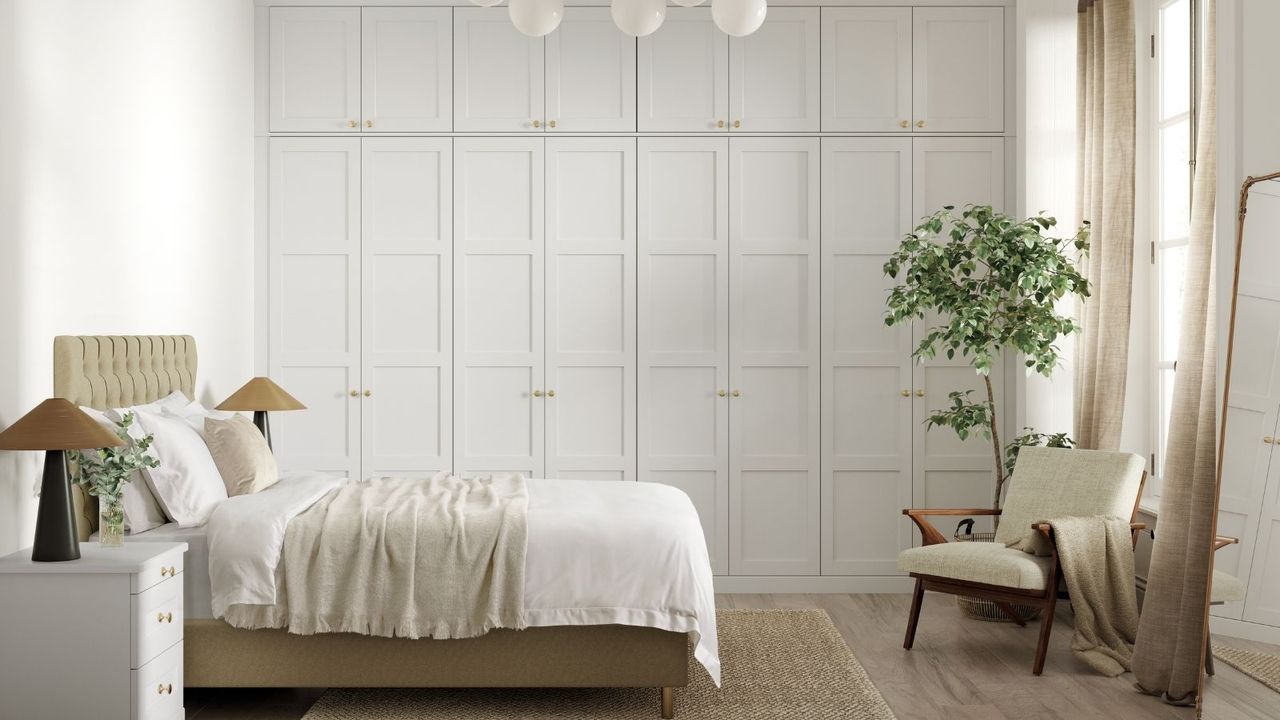 A white bedroom with light wood floors, tall mirror and white chair