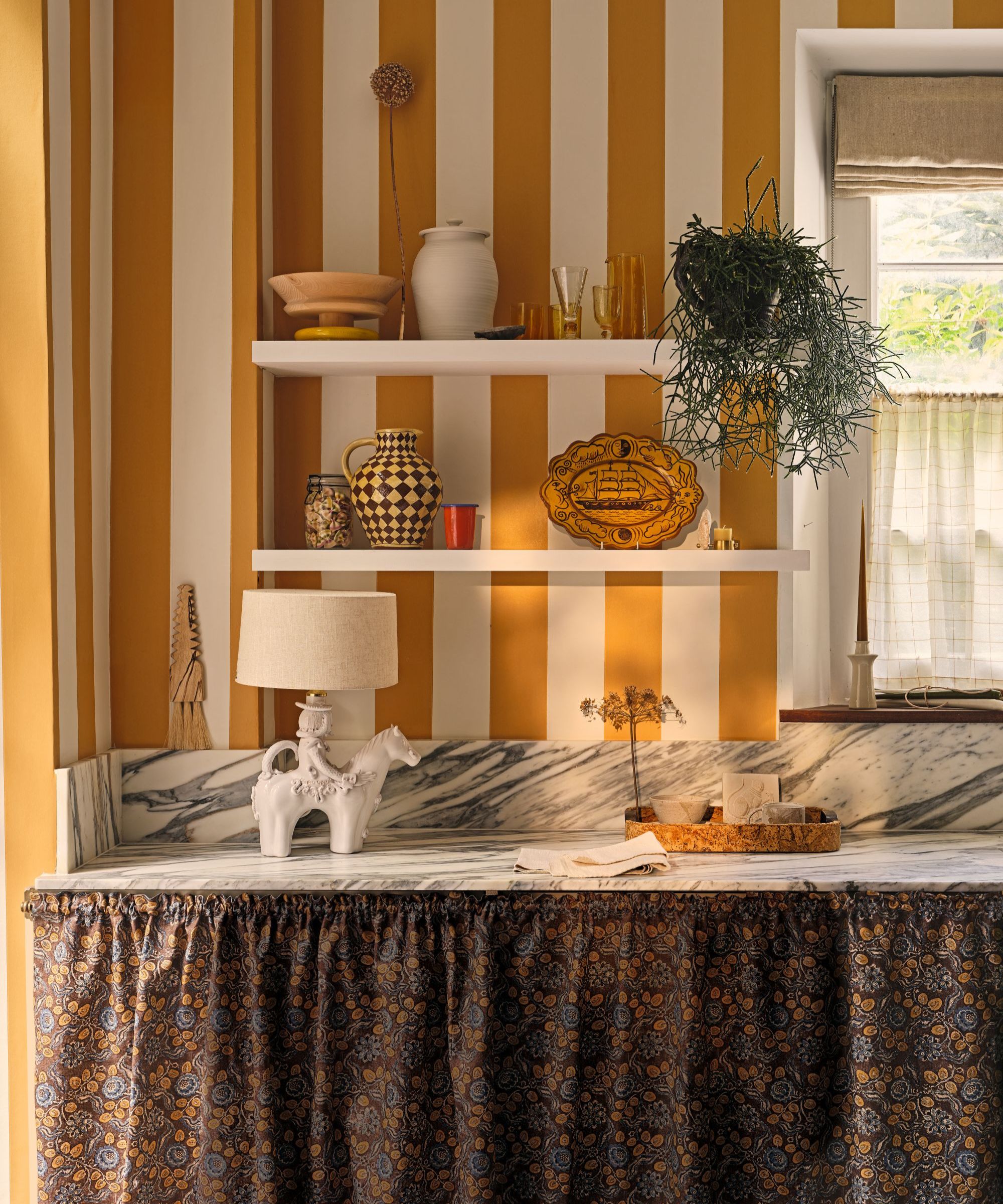 a kitchen countertop with decor on top, a skirt covering the base shelves, two floating shelves with decor on them, and striped wallpaper