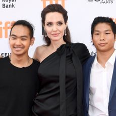 Angelina Jolie poses with two of her sons, Pax and Maddox, while wearing a one-shoulder black dress