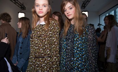 Two female models, one in a blue dress with floral pattern, and one in a brown dress with floral pattern