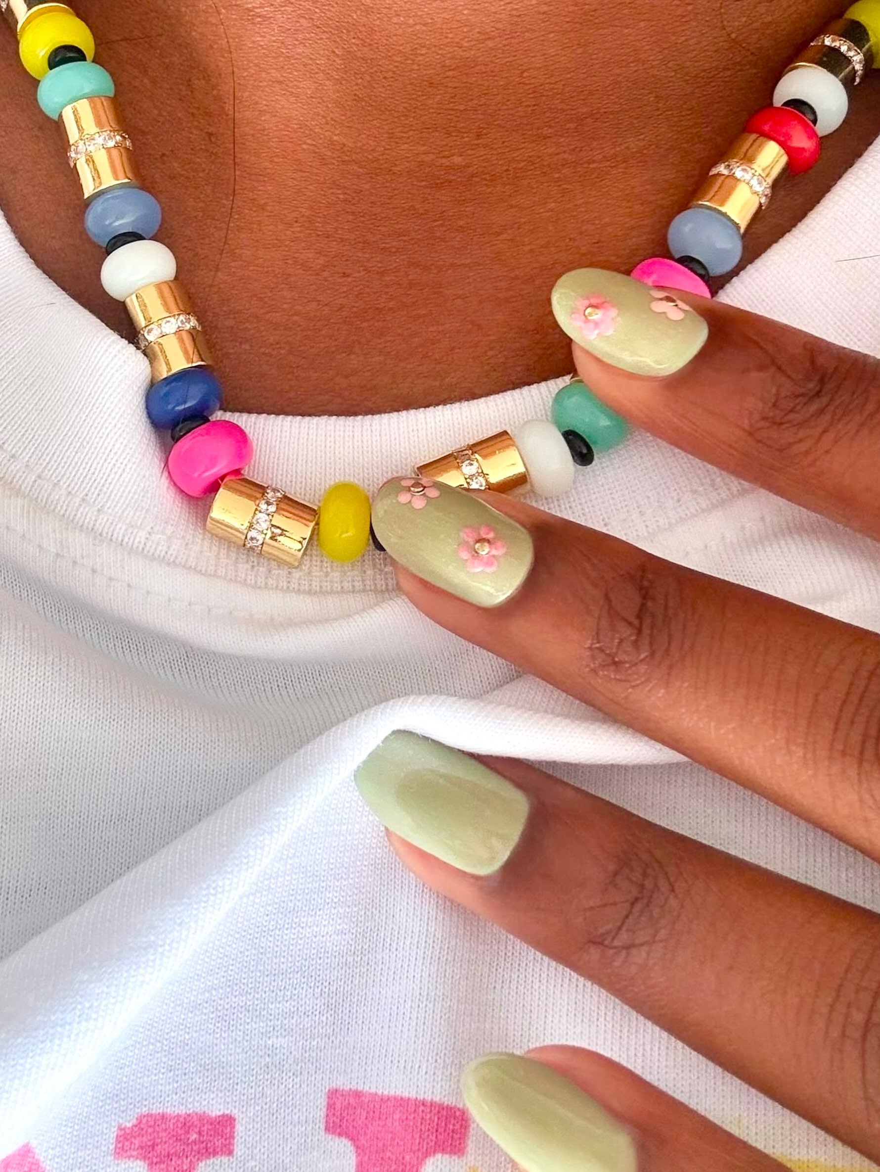 Shimmering jade nails with pink-and-gold chrome flowers, coordinated with a colorful beaded necklace