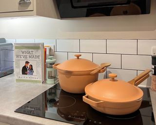 Pink Our Place pans on hob with cookbook in shot in white kitchen