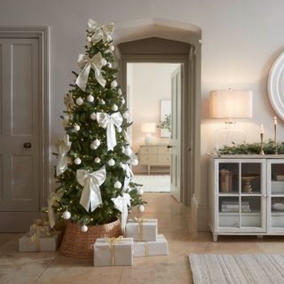 A slim Christmas tree decorated with white baubles and large white bows