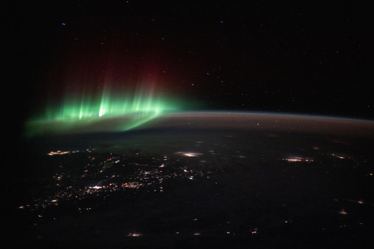 green auroras glow above city lights in a photo taken from the international space station