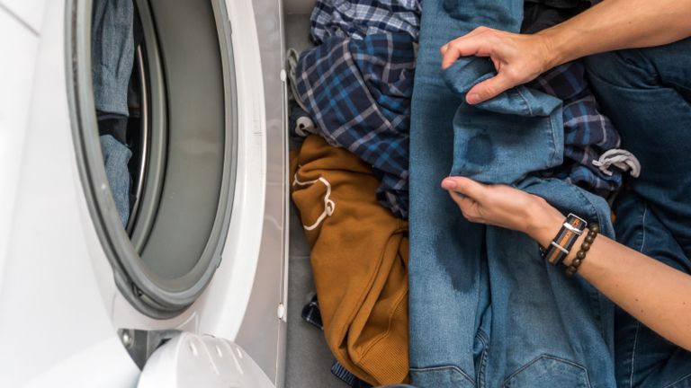 how to remove grease stains - person with stained jeans by a washing machine - GettyImages-1219375328