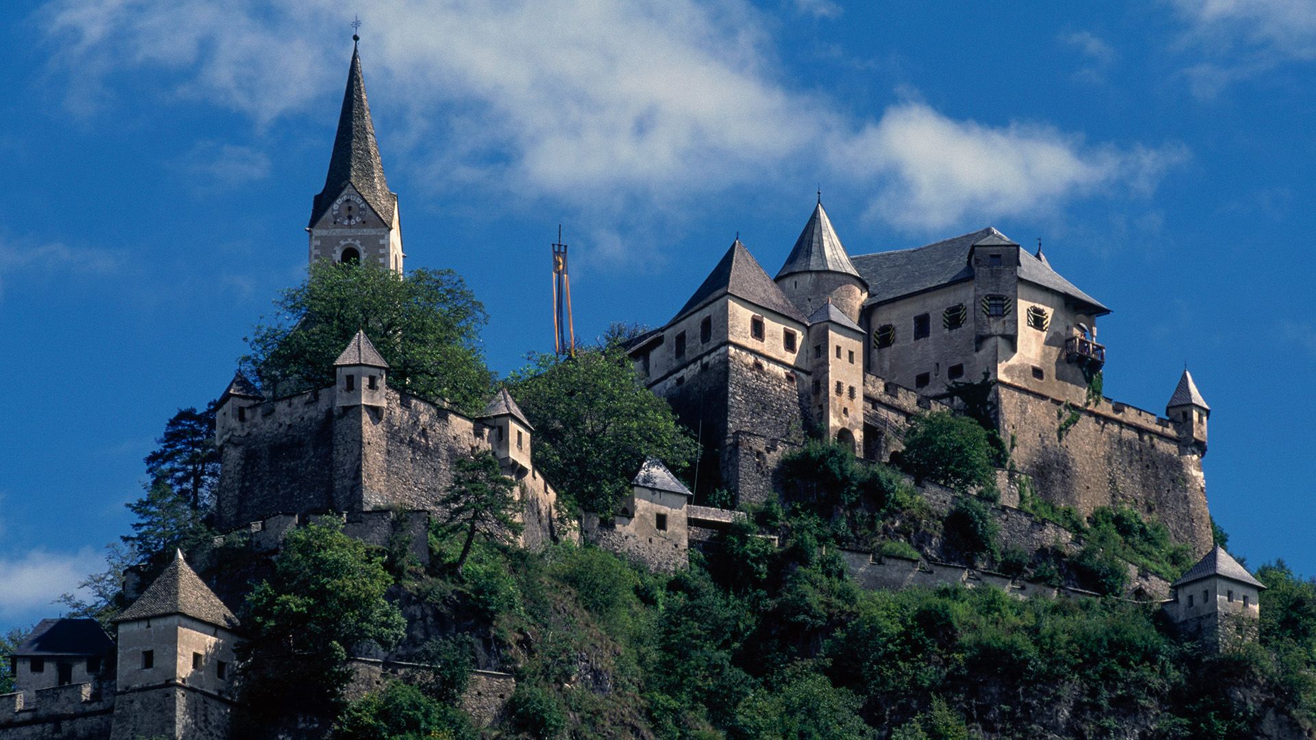 A close up of a series of stone towers and walls on top of a large hill.