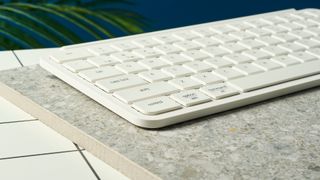 a close up shot from the side of a white wireless bluetooth keyboard resting on a clean white table