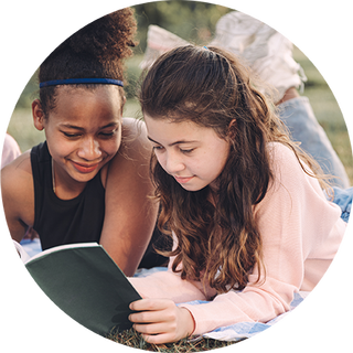 Image of two girls lying on the grass reading a book