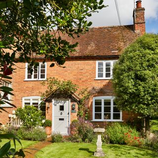 exterior of a red brick victorian cottage with a age green front door and bird bath in garden