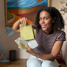 Woman in striped top holding fabric samples, sitting in front of landscape painting