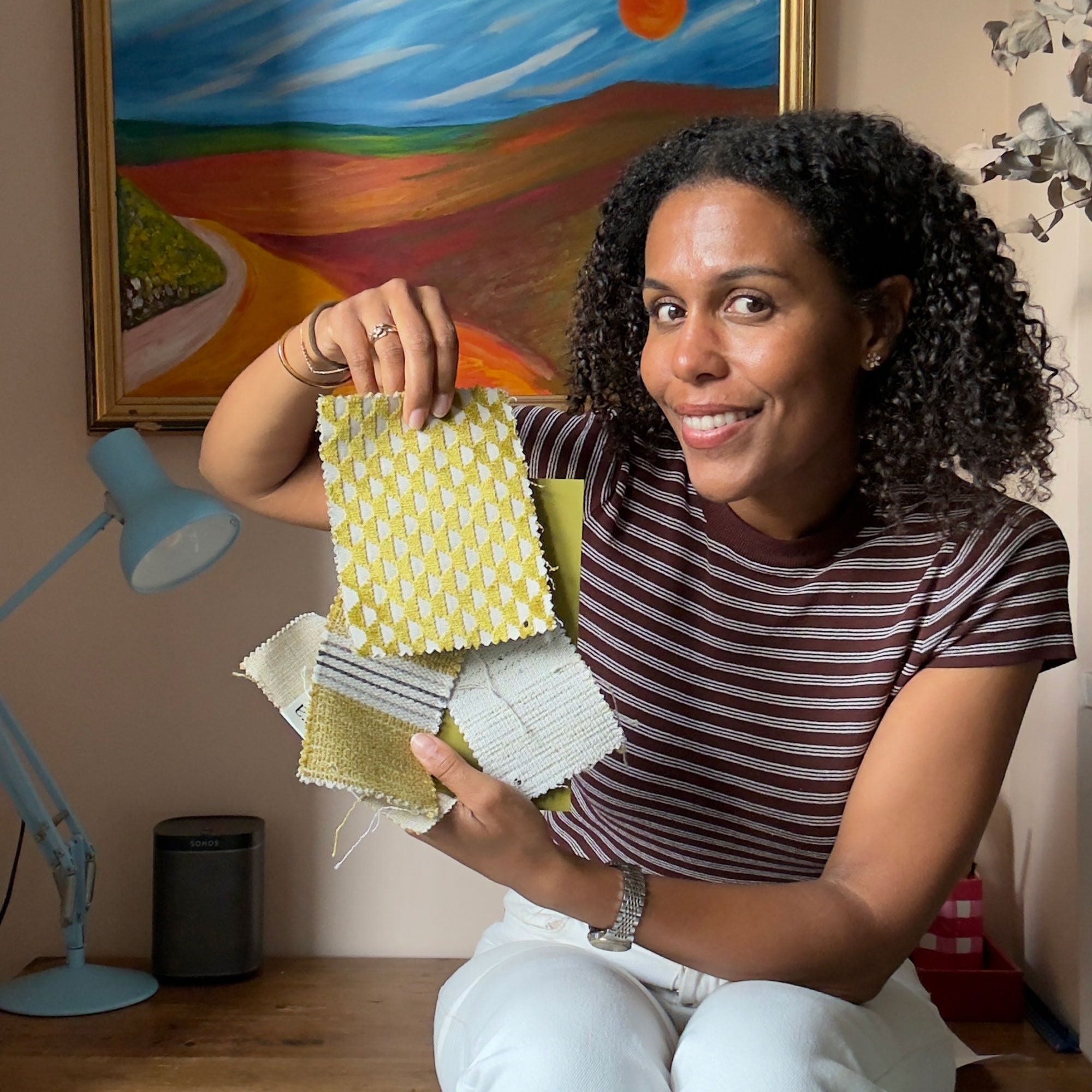 Woman in striped top holding fabric samples, sitting in front of landscape painting