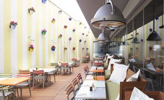 Dining area of Mama Shelter hotel, Istanbul with stiped walls and chairs, industrial lights and flower pots on the walls