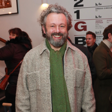 Michael Sheen wearing green scraf and grey coat.
