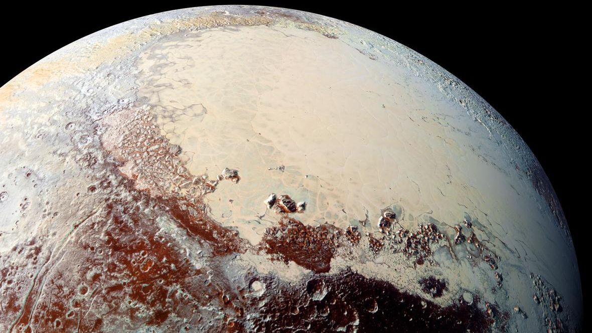 up-close spacecraft photo of pluto, showing a large, heart-shaped expanse of yellowish ice surrounding by reddish-brown hills