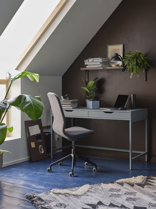 home office in loft, blue painted floorboards, desk under eaves, chair, shelf, rug, plants
