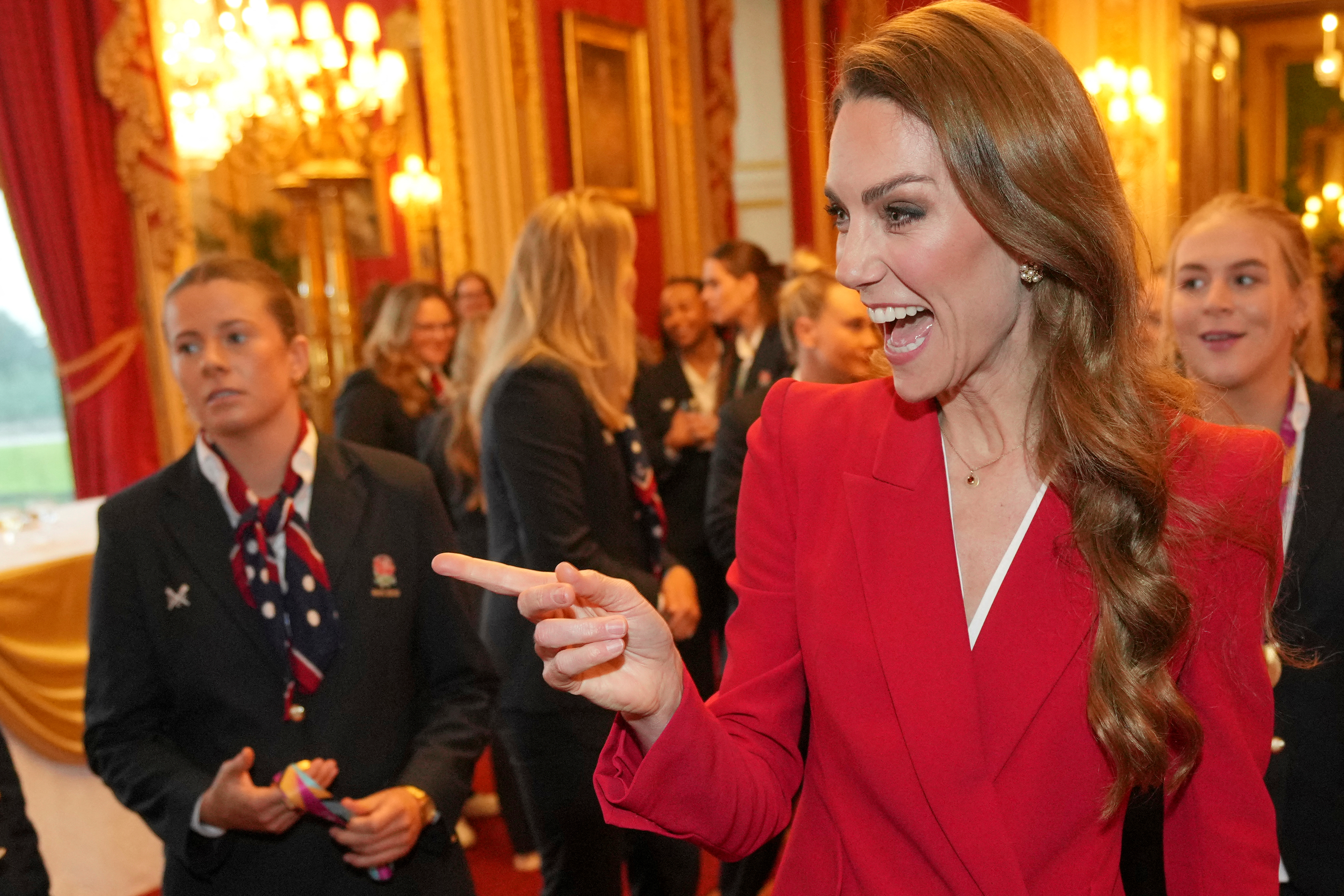 Princess Kate wearing a red suit and pointing at a reception with England rugby team