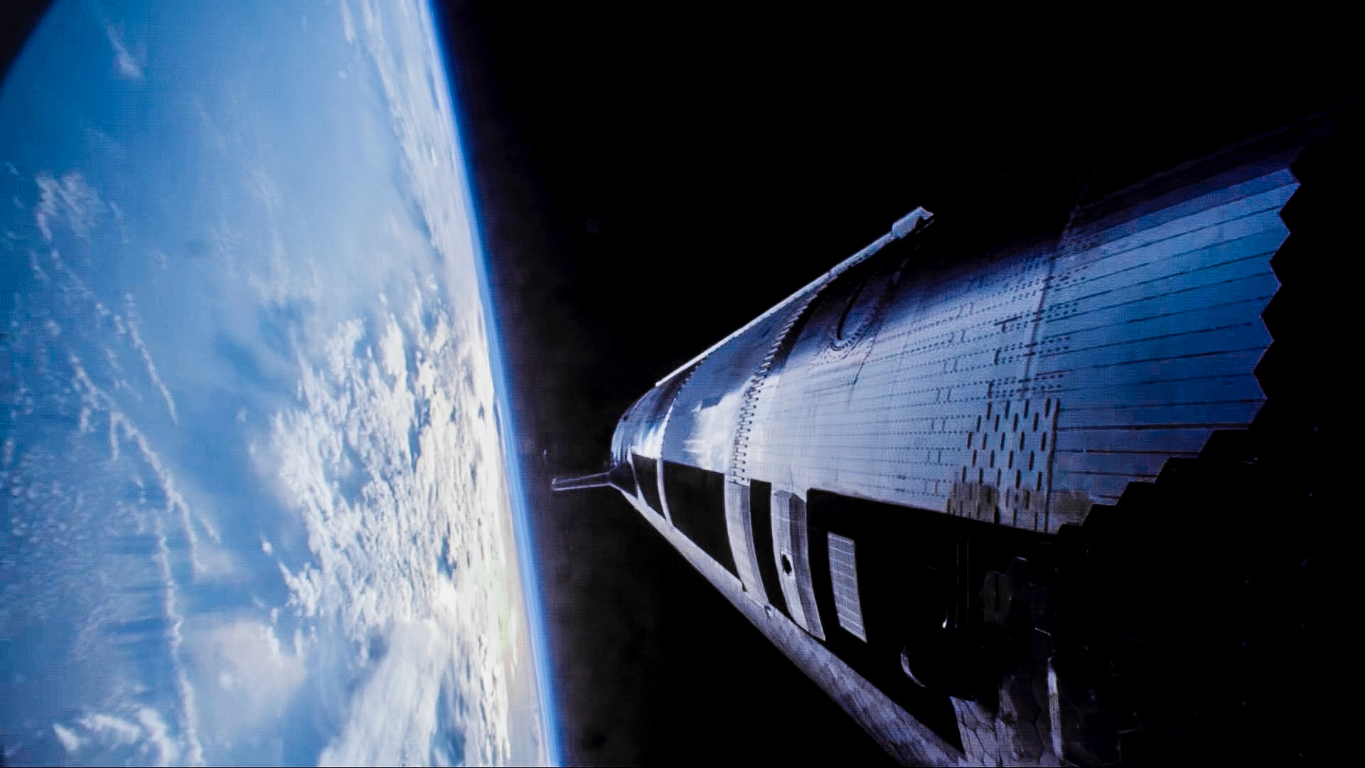 a large, cylindrical, silver metallic spaceship flies in earth orbit