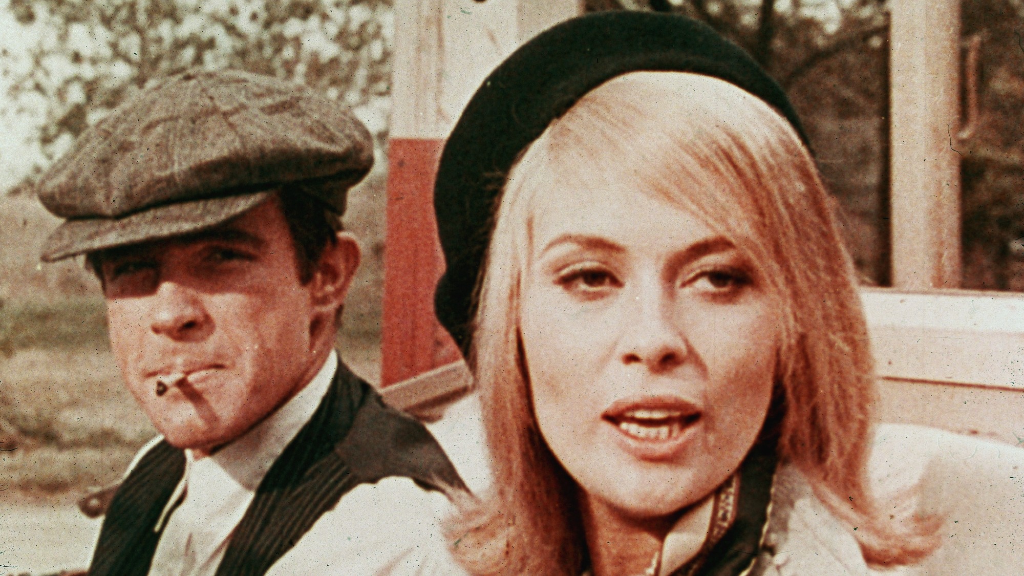 front shot of Warren Beatty (with a cigarette in his mouth) next to Faye Dunaway in an askew black beret. it's a still from the 1967 movie Bonnie and Clyde